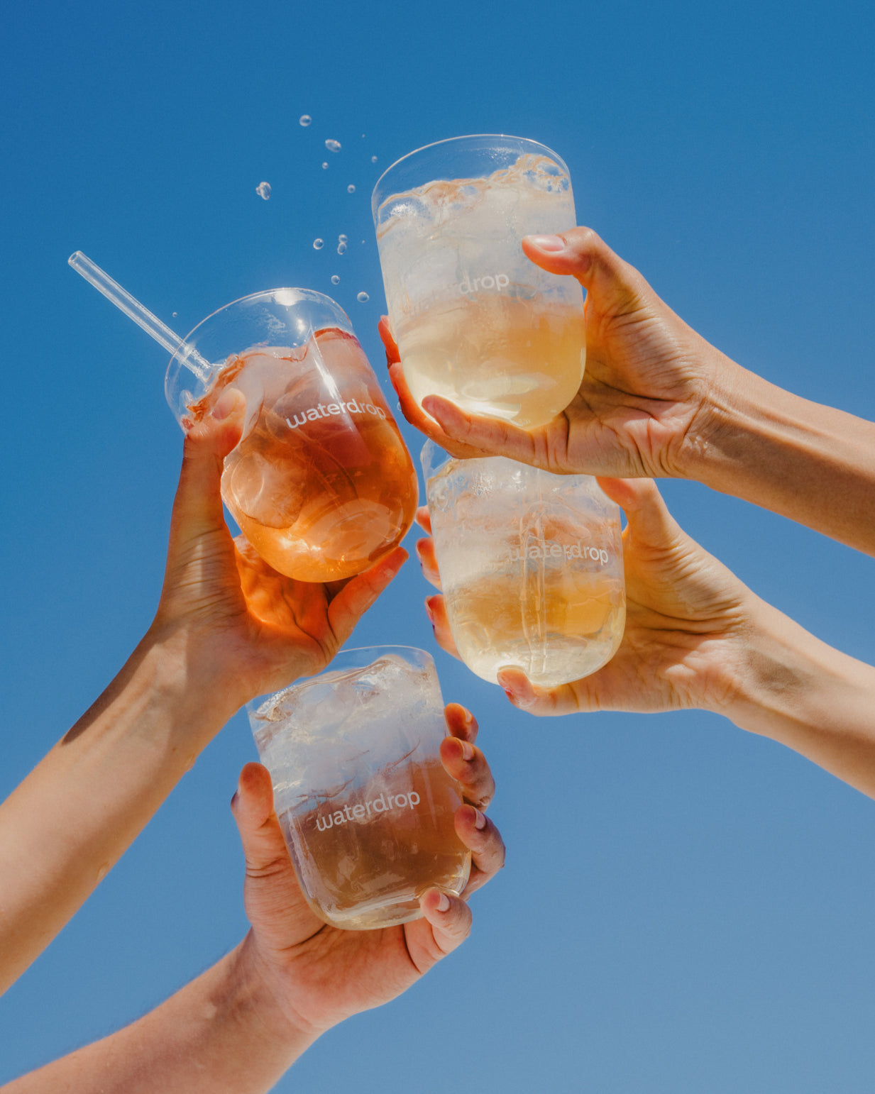 Hands holding glasses of iced tea, showcasing the ICE TEA Set from waterdrop® with flavors: Lemon, Peach, Blueberry, and Raspberry.