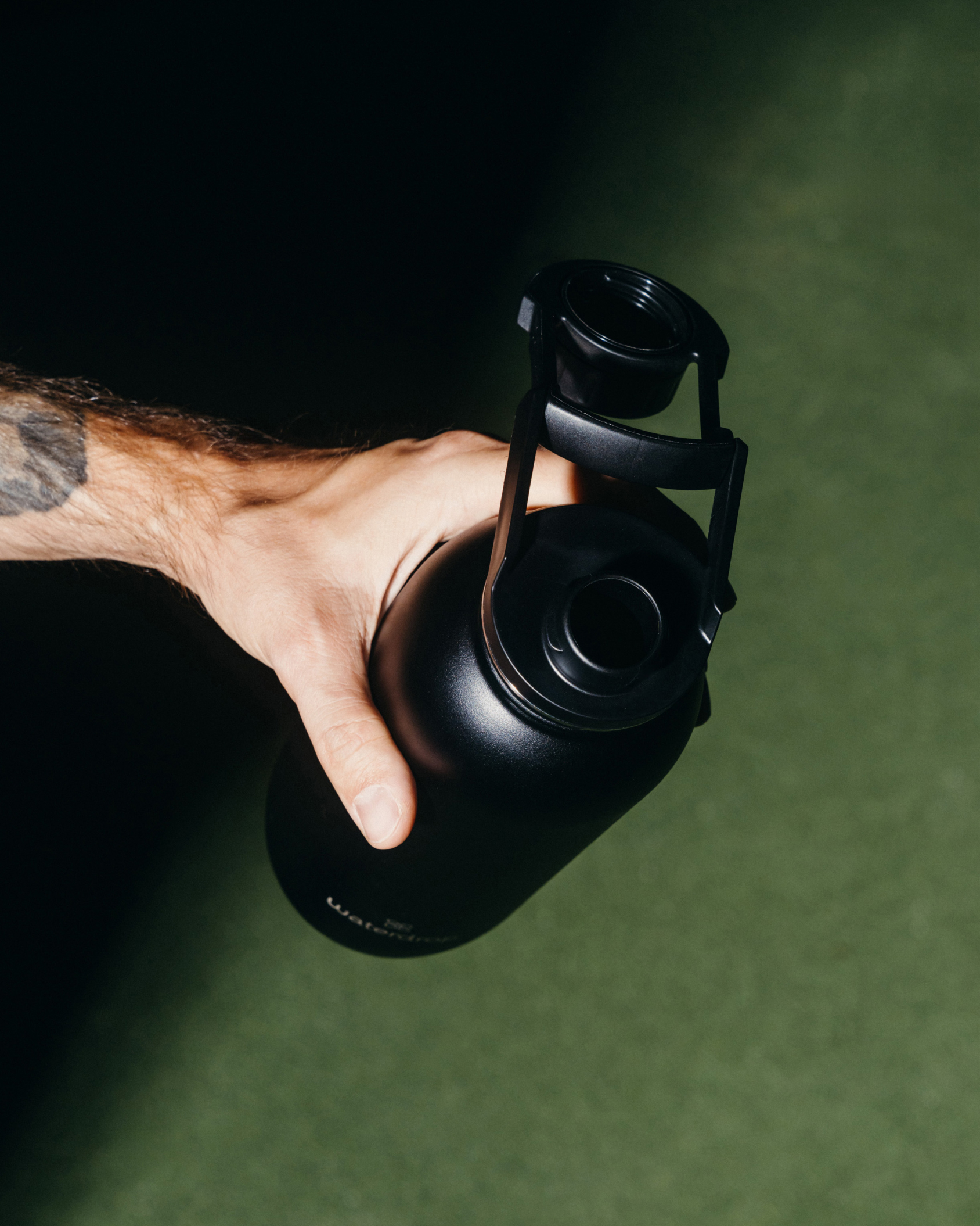 Hand holding a black water bottle with an attached Swing Lid, ensuring hygienic sips and lid security. Suitable for all-purpose hydration.