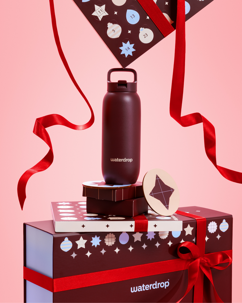 Black water bottle with a looped lid sits on stacked gift boxes tied with red ribbons against a pink background.