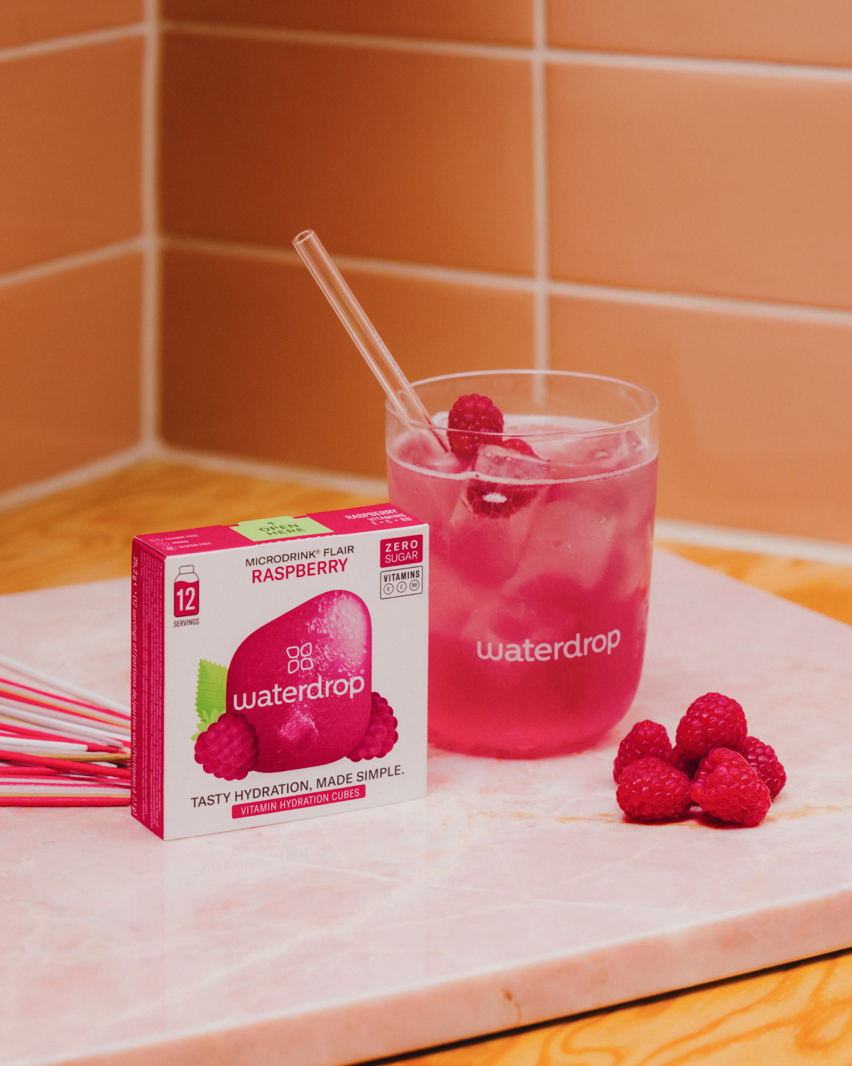 RASPBERRY Microdrink box beside a glass of pink drink with ice and raspberries, highlighting the fresh, sweet raspberry flavor.