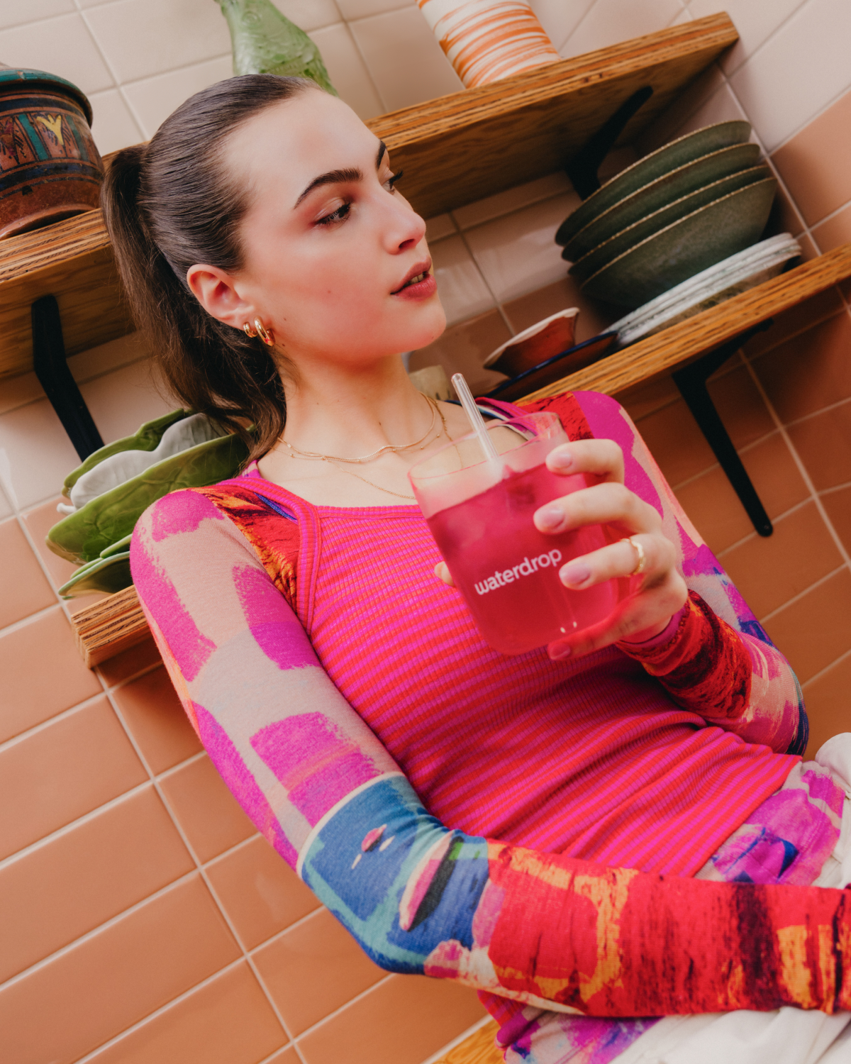A woman enjoying a drink with a straw, likely savoring the raspberry-flavored hydration cubes from waterdrop®.
