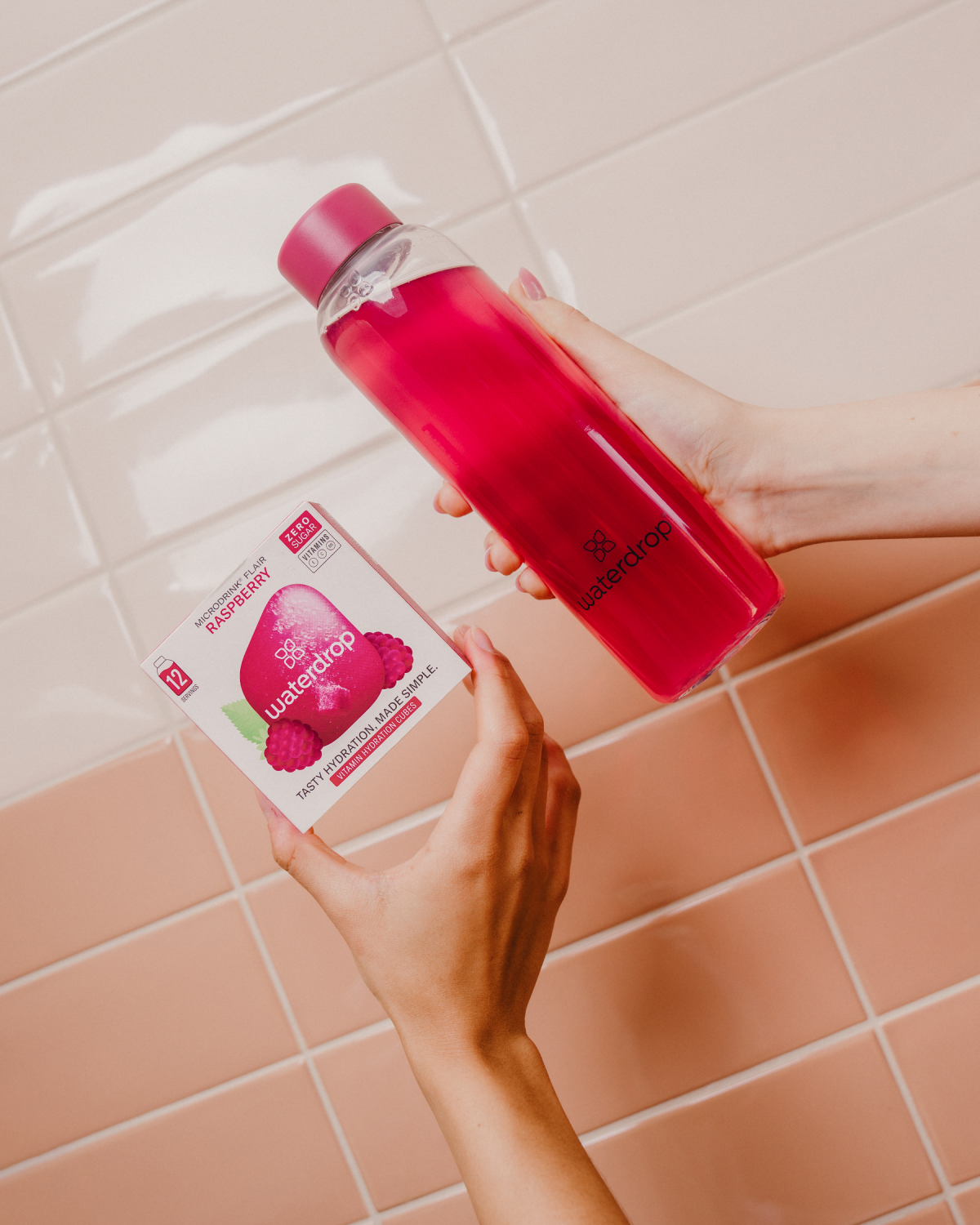 Person holding a bottle of liquid and a box of waterdrop® RASPBERRY flavored hydration cubes.